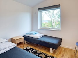 Una habitación pequeña con cama individual, ventana, mesita de noche y una silla.