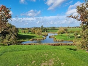 A golf course with a pond, trees, and a clear sky. - 9 Person Holiday Home in Skibby (Skibby)