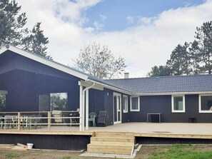 A modern building with a dark exterior, a covered outdoor area with a wooden deck, and a clear sky. - 9 Person Holiday Home in Skibby (Skibby)