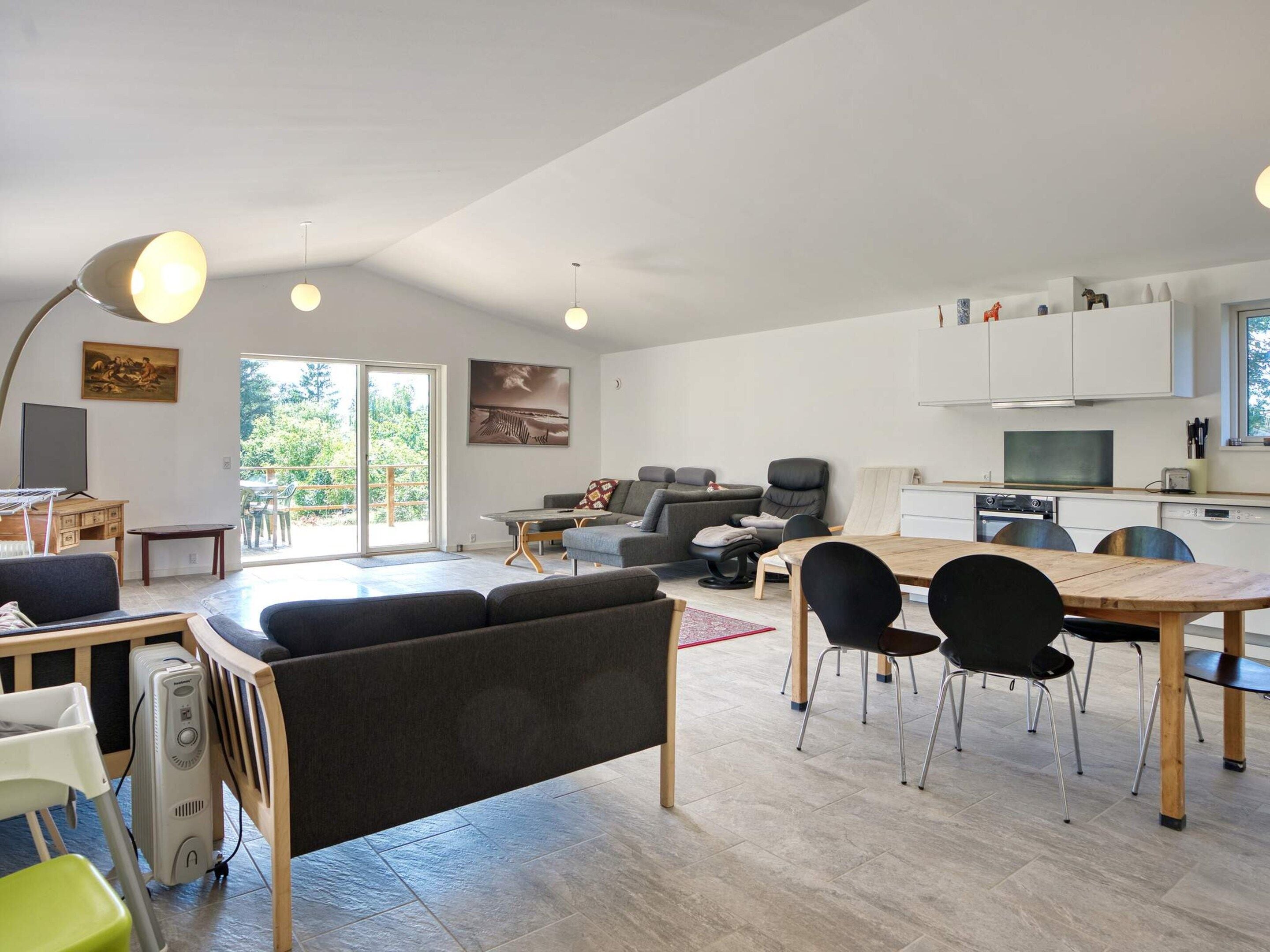 A spacious living area with a sofa, dining table, chairs, and a kitchen area with cabinets and appliances.