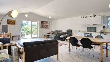 A spacious living area with a sofa, dining table, chairs, and a kitchen area with cabinets and appliances.