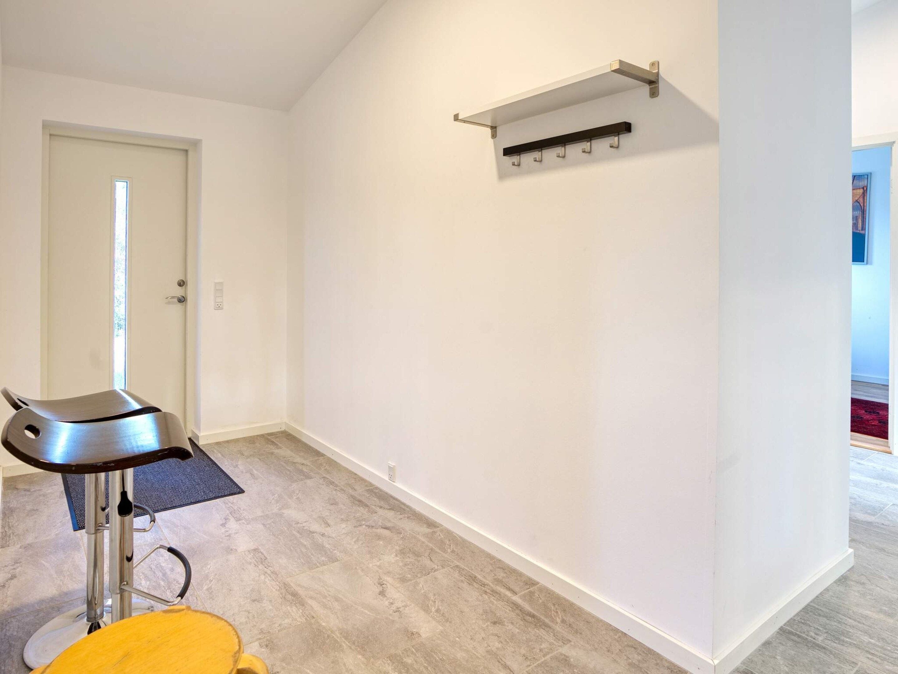 A room with a modern chair, a coat rack, and a door.