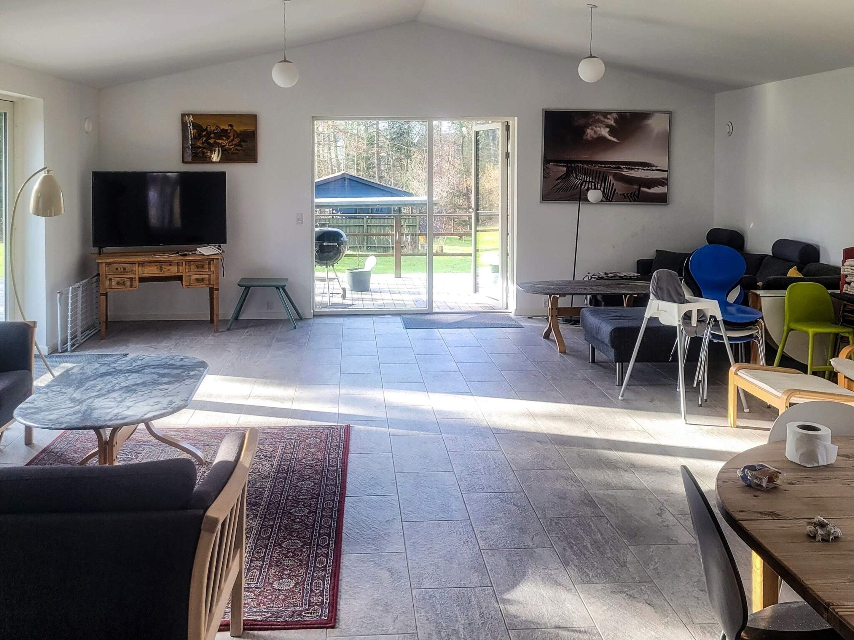 Ein geräumiges Wohnzimmer mit Fernseher, Sitzgelegenheiten, Kamin und Blick ins Freie durch die Glasdoor.