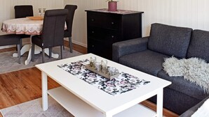 Una sala de estar acogedora con un sofá gris, una mesa de centro blanca con mantel individual estampado, y un comedor con mesa y sillas.