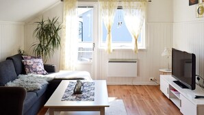 Una sala de estar acogedora con un sofá, una mesa de centro, un televisor en un mueble bajo y una ventana con cortinas.
