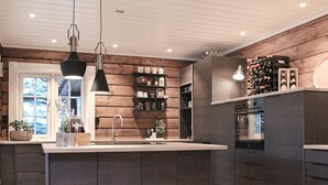 A modern kitchen with a central island, dark cabinetry, wooden wall paneling, and a wine rack. - 5 Star Holiday Home in Geiranger (Stranda)