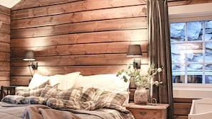A cozy bedroom with a wooden headboard, a bed with plaid bedding, two bedside lamps, and a nightstand with a vase and candle. - 5 Star Holiday Home in Geiranger (Stranda)