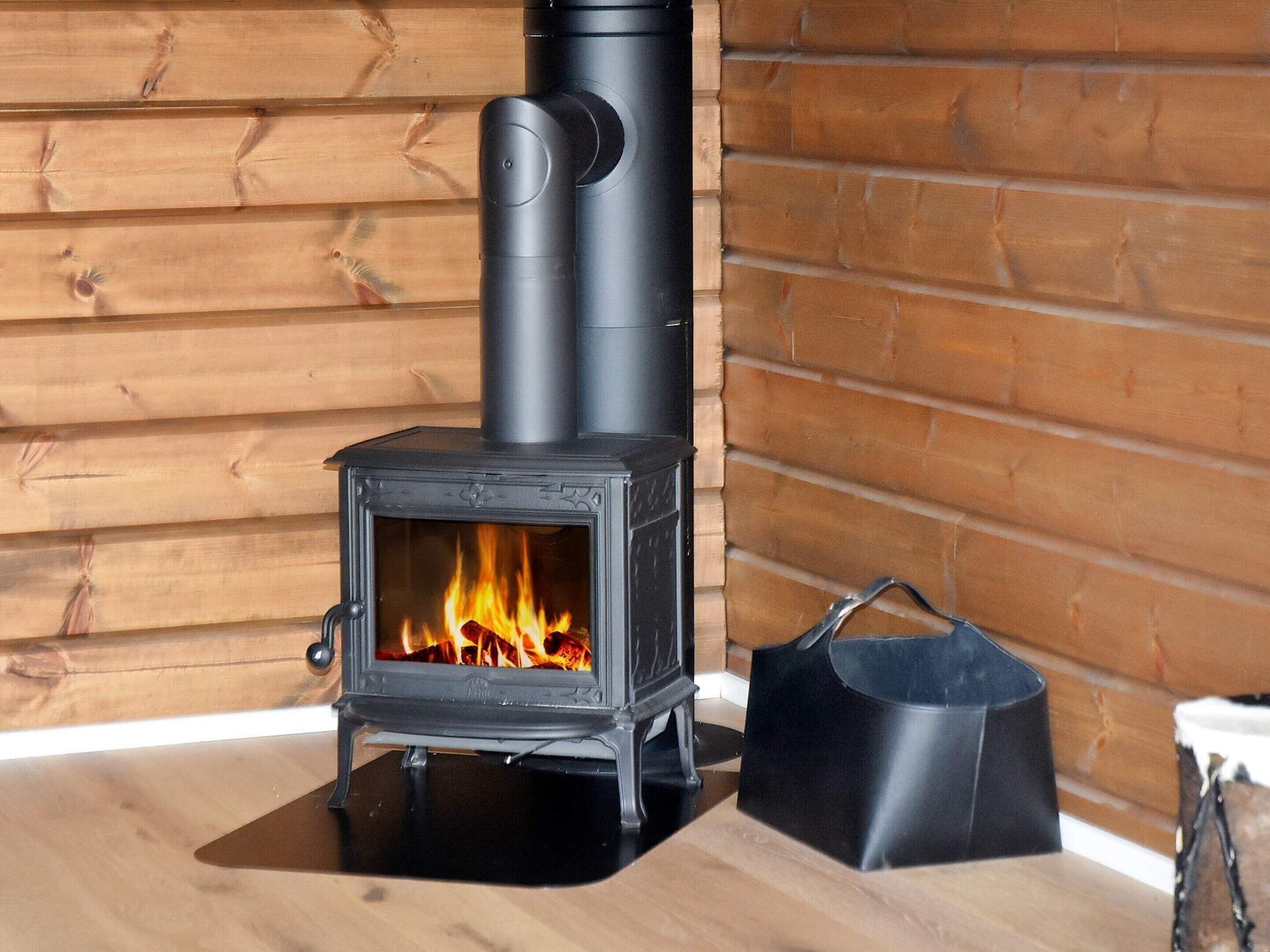 A wood-burning stove with a glass door, a black chimney, and a black bag beside it.