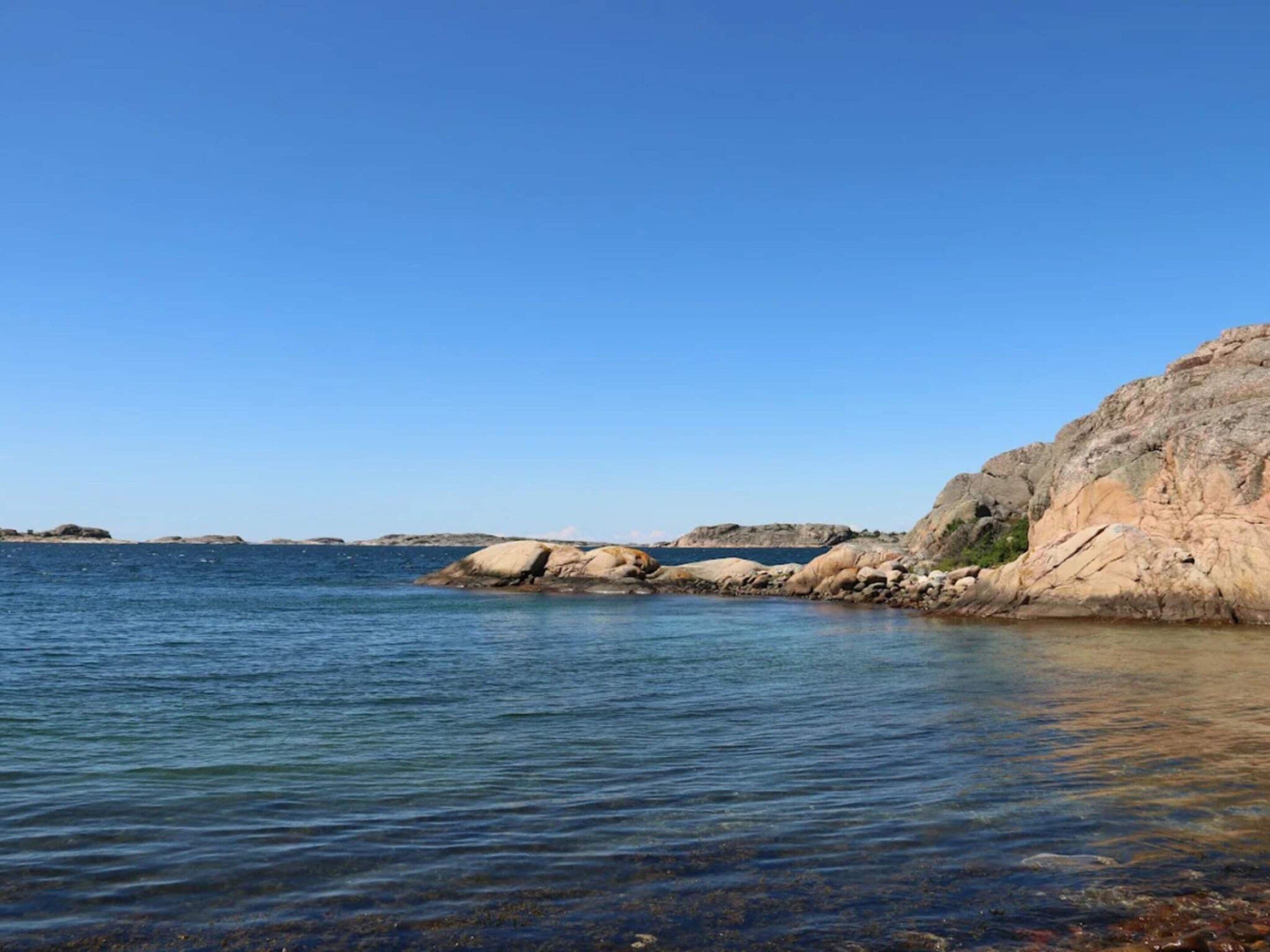 Ett kustlandskap med klart vatten, klippformationer och land i fjärran.