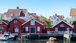 Een rij rode houten huizen met puntgevels, aangemeerde boten, en een heldere blauwe lucht.