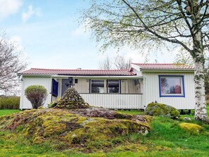 Une petite cabane blanche avec un toit rouge, une véranda et une structure en pierre à l’avant.