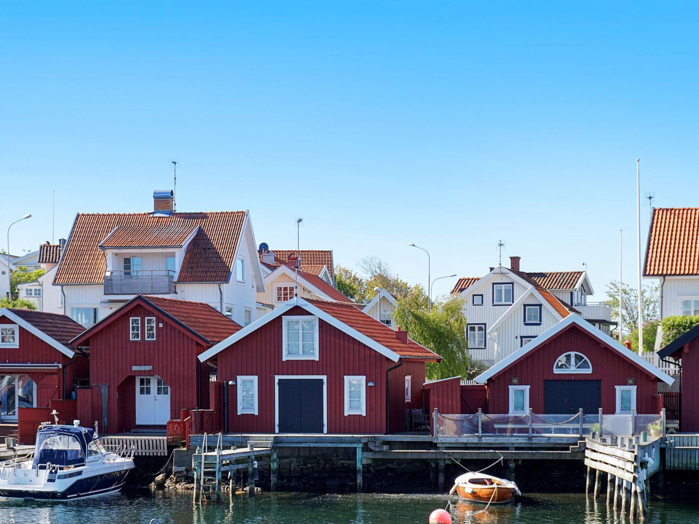 A row of red wooden houses with gabled roofs, docked boats, and a clear blue sky.