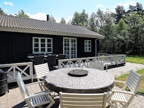 An outdoor patio with a round table and chairs, a wooden deck, and a building with windows and a chimney. - 5 Star Holiday Home in Laeso (Læsø)
