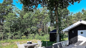 En træterrasse med udendørs møbler, et lille skur og et træ i baggrunden.