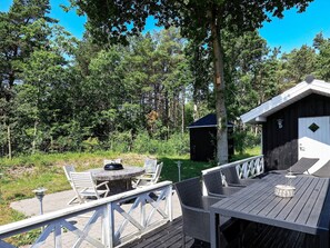 En träaltan med utemöbler, ett litet förråd och ett träd i bakgrunden.