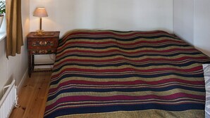 A room with a bed covered in a striped blanket, a bedside table with a lamp, and a window with curtains. - 4 Person Holiday Home in Farentuna (Faerentuna)