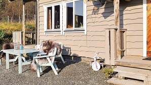 A rustic cabin with a wooden exterior, a gravel patio, a table with chairs, and a bicycle.