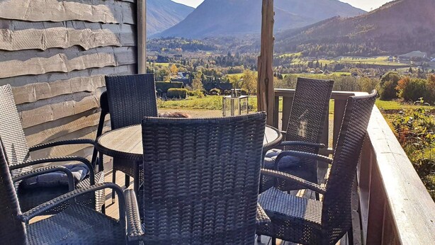 A balcony with wicker chairs and a table overlooking a mountainous landscape.