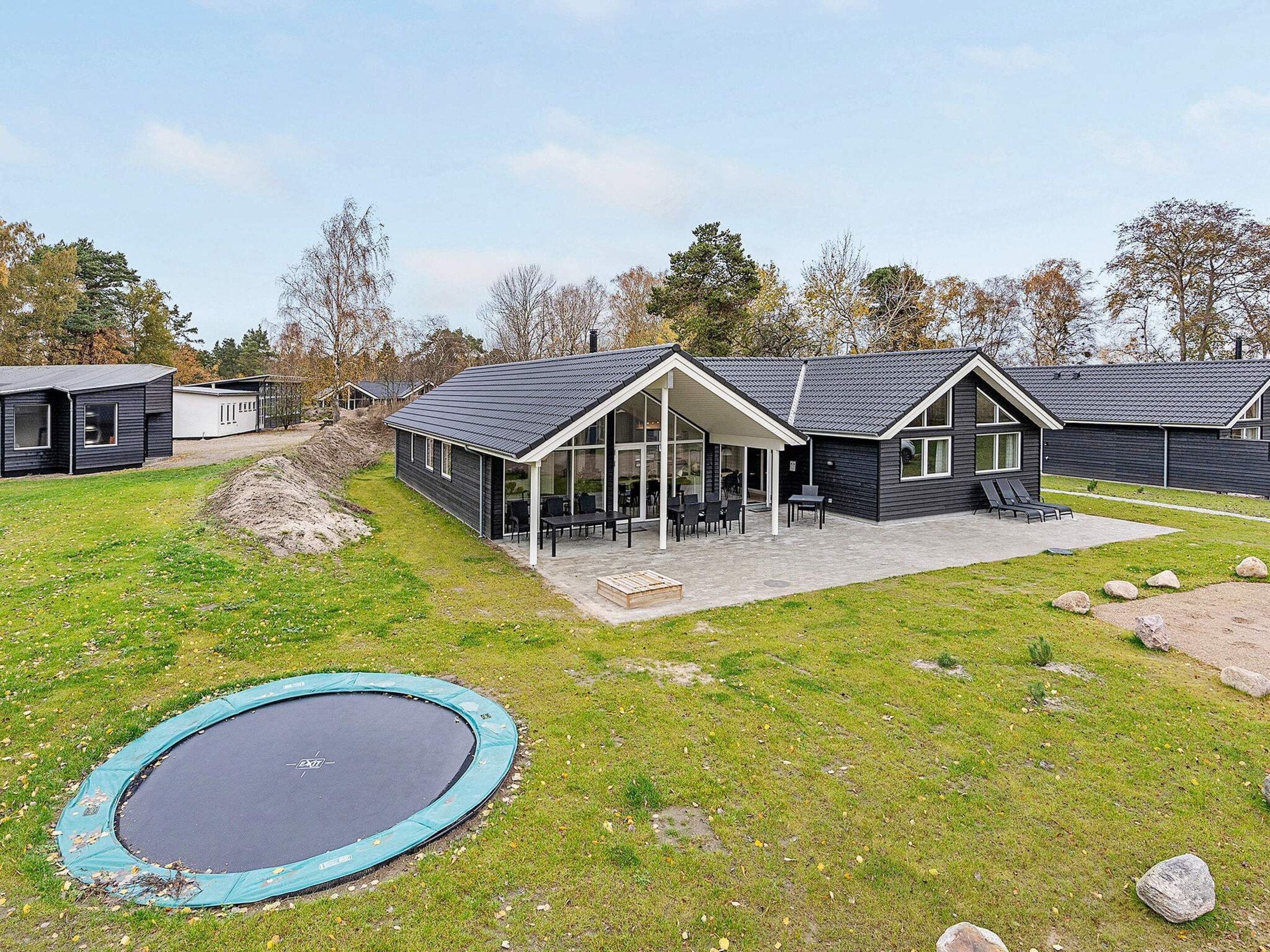 Una casa moderna con un porche cubierto, un trampolín y un patio con césped.