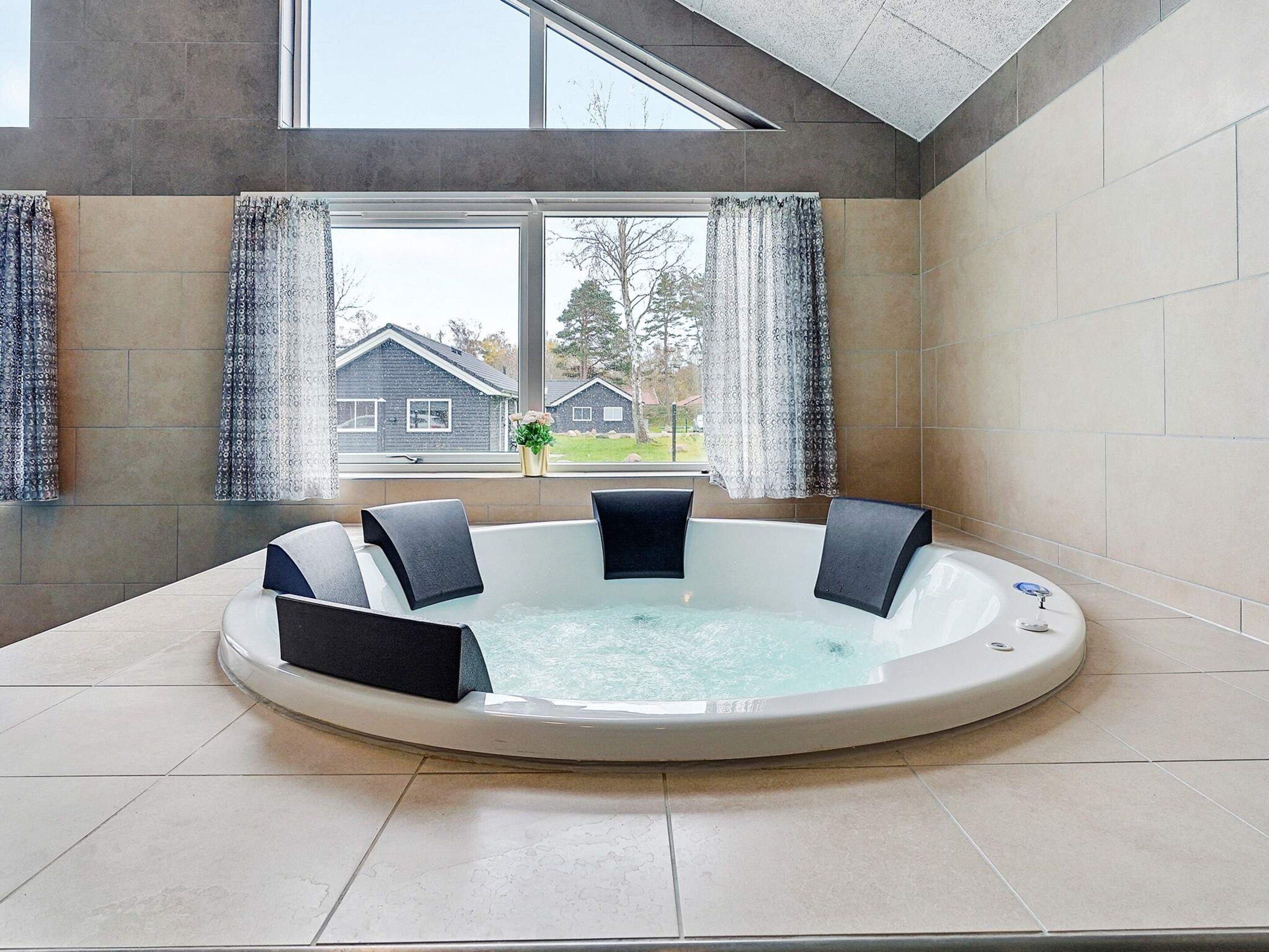 A hot tub with four black chairs, a window with curtains, and a view of houses outside.