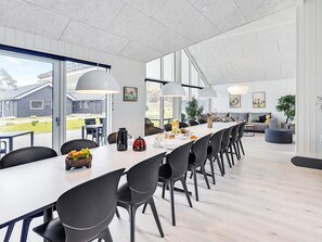 A modern dining area with a long table, black chairs, and pendant lights.