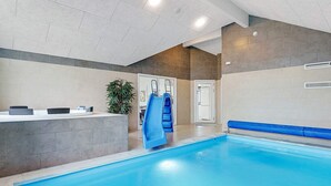 An indoor swimming pool with a blue slide, a reception desk, and a potted plant. - 5 Star Holiday Home in Vaeggerlose (Vaeggerlose)