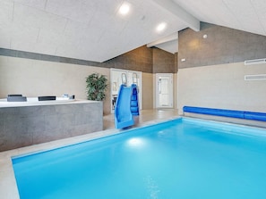 An indoor swimming pool with a blue slide, a reception desk, and a potted plant. - 5 Star Holiday Home in Vaeggerlose (Vaeggerlose)