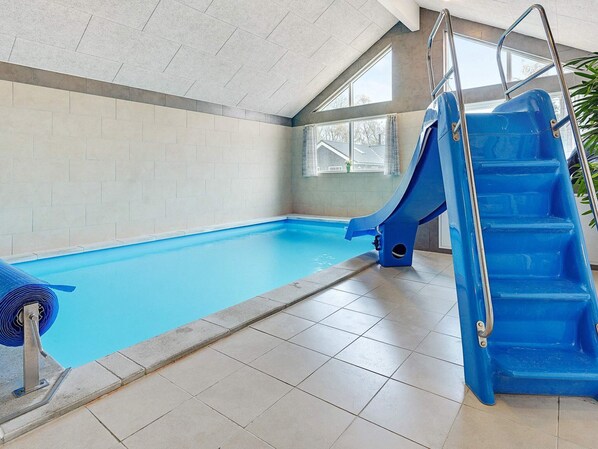An indoor swimming pool with a blue slide and a ladder.