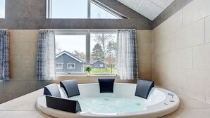 A hot tub with seating, a window with curtains, and a view of houses outside. - 5 Star Holiday Home in Vaeggerlose (Vaeggerlose)