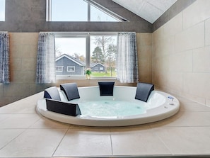 A hot tub with seating, a window with curtains, and a view of houses outside. - 5 Star Holiday Home in Vaeggerlose (Vaeggerlose)