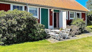 A red house with a tiled roof, a green door, and a small patio with a table and chairs. - 4 Star Holiday Home in Ellos (Ellos)
