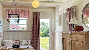 A cozy kitchen with wooden cabinets, a dining table with chairs, a hanging light fixture, and a view of the outdoors. - 4 Star Holiday Home in Ellos (Ellos)