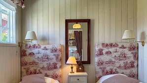 A room with two beds, a nightstand with a lamp, a mirror, and patterned wallpaper. - 4 Star Holiday Home in Ellos (Ellos)