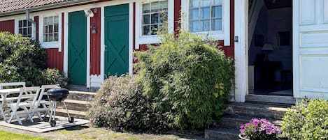 A red and white house with a tiled roof, a green door, and a wooden deck with outdoor furniture.