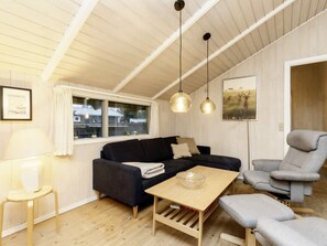 A cozy living room with a dark sofa, a light wooden coffee table, a grey armchair, and a lamp.