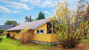 Een geel huis met een schuin dak, een schoorsteen en een raam.