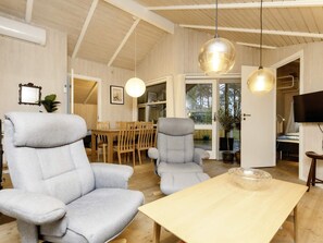 A spacious room with two grey armchairs, a wooden dining table, and pendant lights.