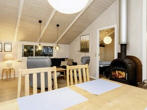 A cozy room with a wooden ceiling, a fireplace, a sofa, a dining table, and hanging pendant lights.