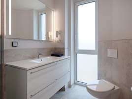Et stilfuldt badeværelse med hvid vask, spejl, håndklæde og toilet.