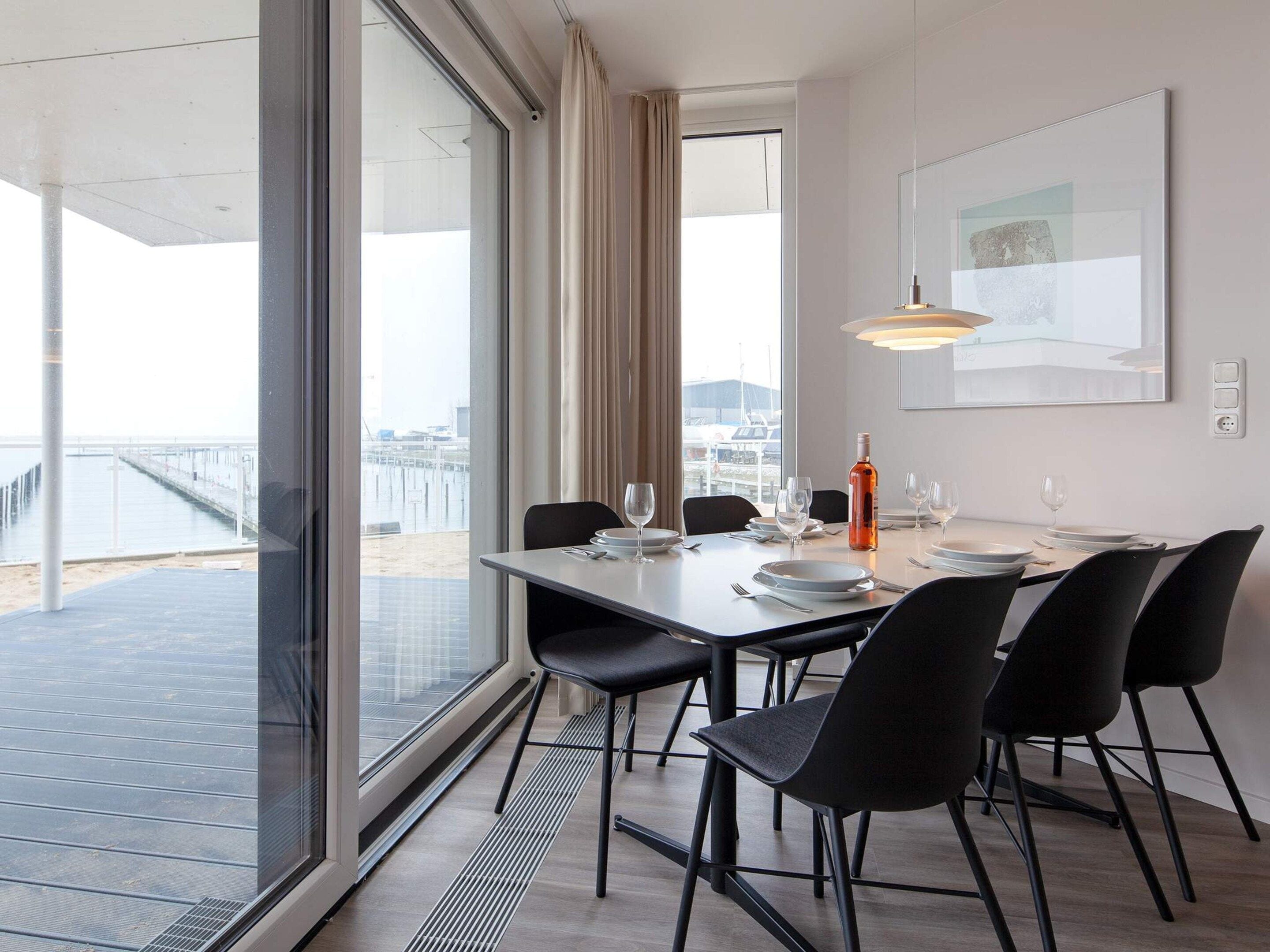 A dining area with a table set for four, large windows, and a view of a pier.