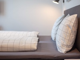 Una cama con cabecera, dos almohadas y una lámpara de noche.