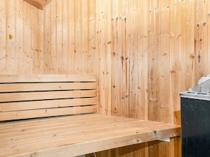 Una sauna de madera con un banco y un calentador negro.