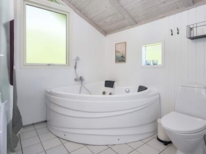 Un baño con una bañera blanca grande, un inodoro y un ventanal que proporciona luz natural.