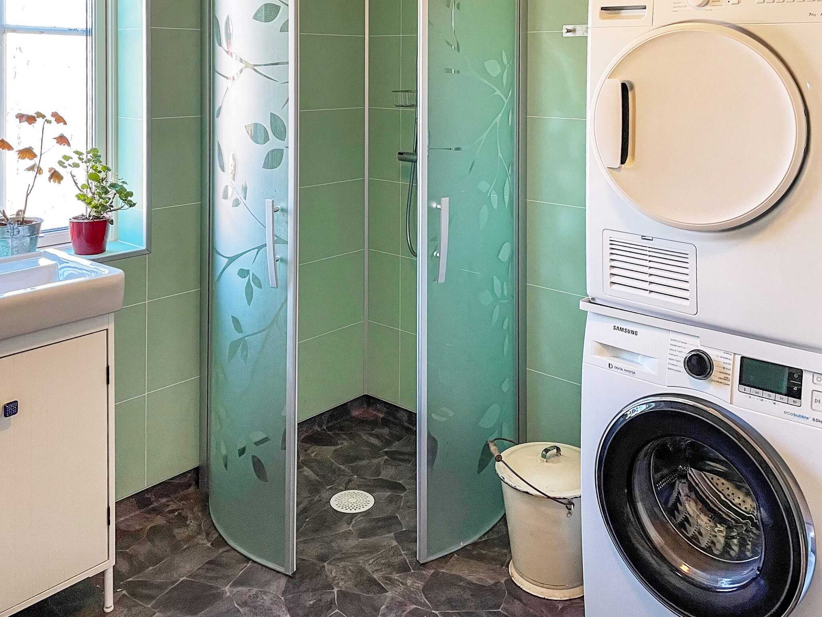 Een wasruimte met een wasmachine, een wastafel en een raam met planten.