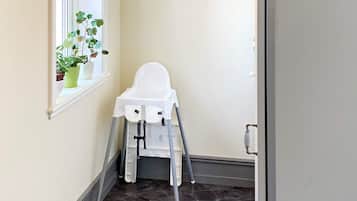 A white high chair in a hallway with a window and potted plants.