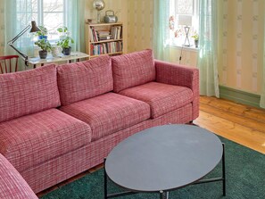 A cozy living room with a red patterned sofa, a small round table, a bookshelf, and a lamp. - 4 Person Holiday Home in Arboga (Arboga)