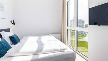 Et moderne hotelværelse med en stor seng, et fladskærms-tv og udsigt over bybilledet gennem store vinduer.