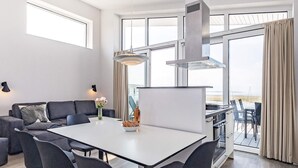 A modern living room with a white dining table, dark chairs, a sofa, and a large window with curtains. - 5 Star Holiday Home in Wendtorf (Lubeck)
