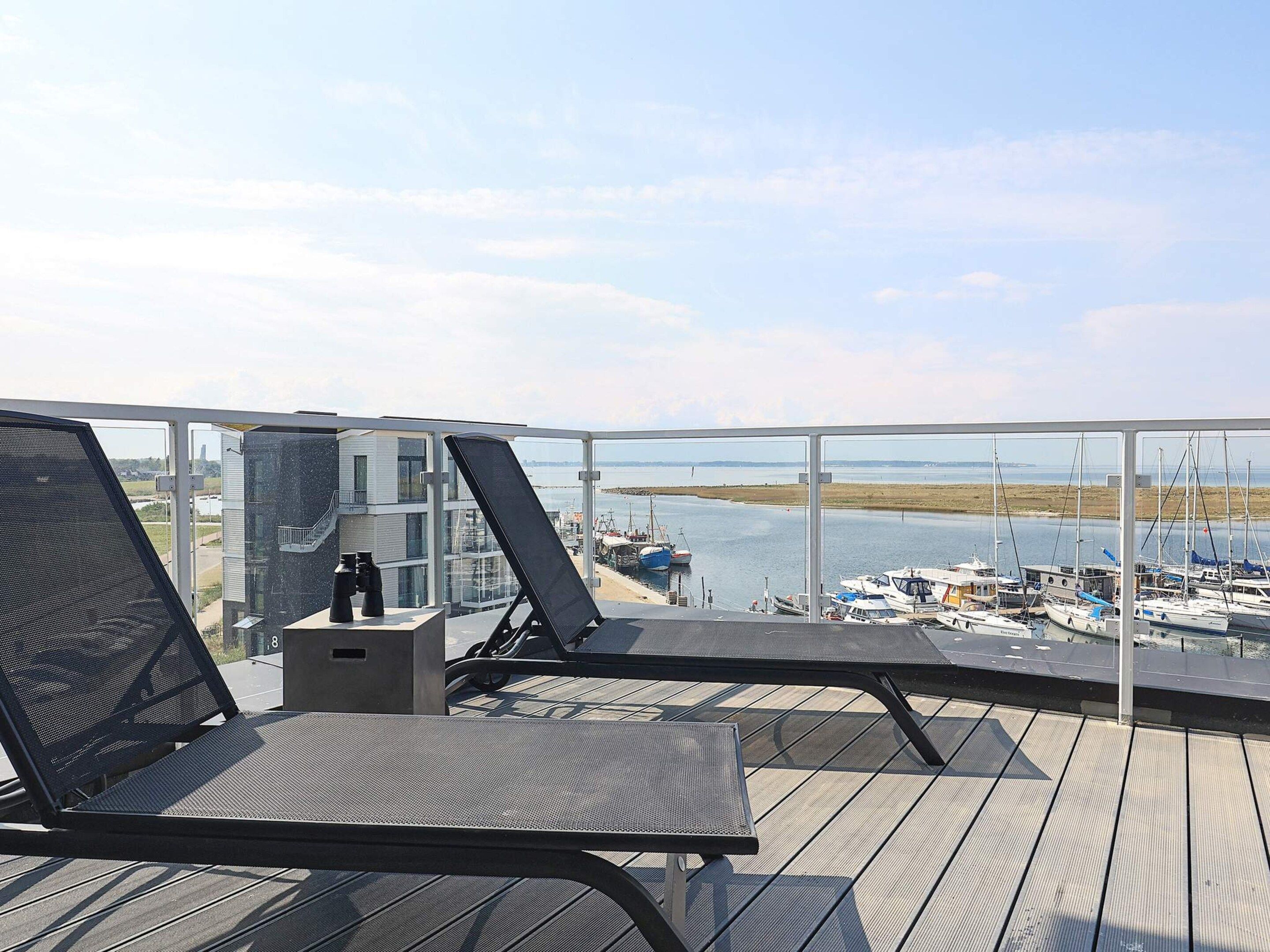 Varanda com duas espreguiçadeiras e uma mesa pequena, com vista para uma marina com barcos.