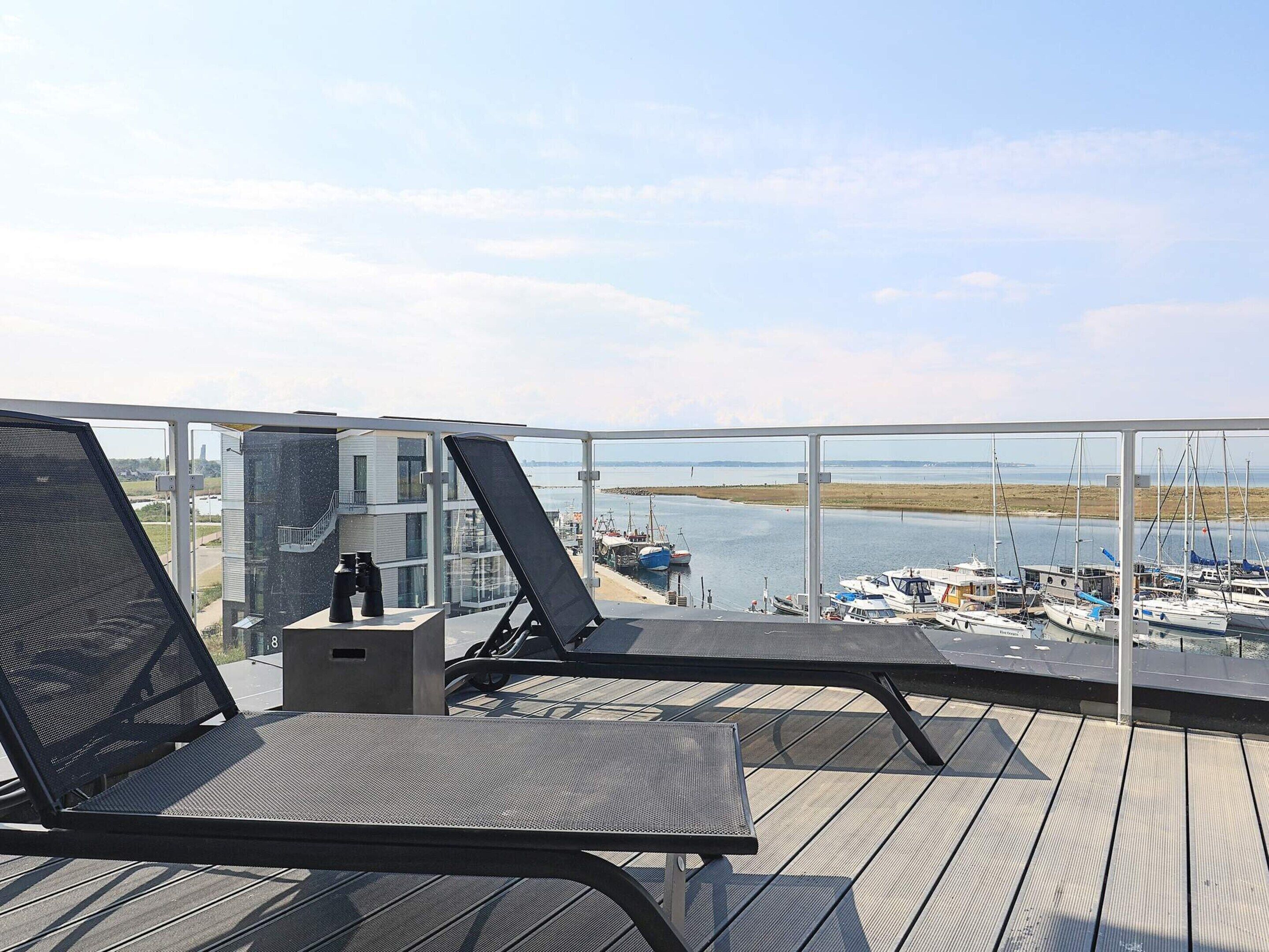 Ein Balkon mit zwei Loungestühlen, einem kleinen Tisch und Blick auf eine Marina mit Booten.